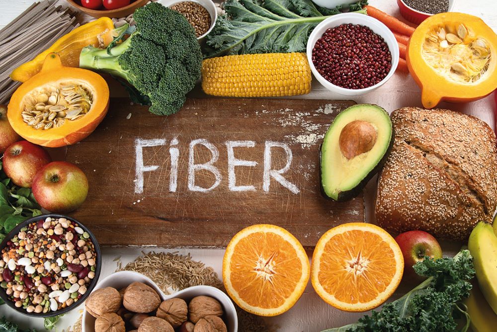 fibre rich foods including fruits, vegetables and grains on a wooden background with a sign reading 'fibre'