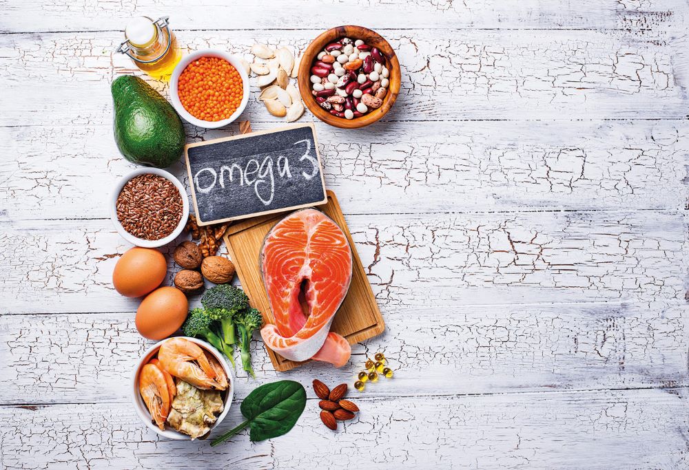omega 3 rich foods including salmon, eggs, pulses and vegetables on a white background