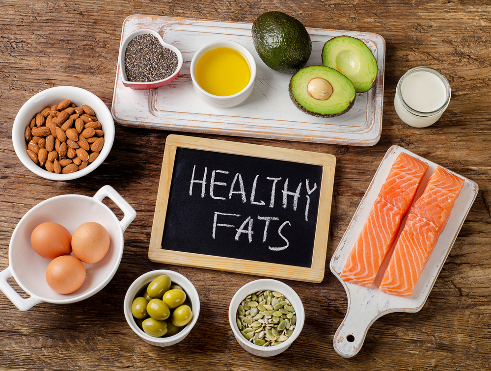 healthy fat sources, including oily fish, eggs, avocado, seeds, on wooden background