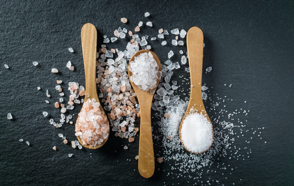 three spoons holding different types of salt, including raw salt, pink Himalayan salt and table salt