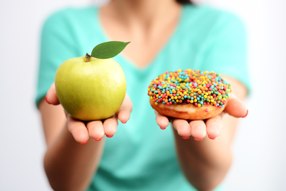 woman holding apple in one hand, doughnut in the other, demonstrating healthy verses unhealthy sugar sources