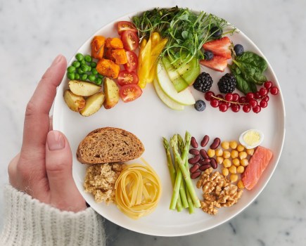 woman holding a balanced eatwell plate of food with vegetables, fruit, grains, protein