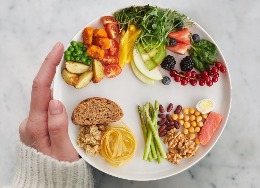 woman holding a balanced eatwell plate of food with vegetables, fruit, grains, protein