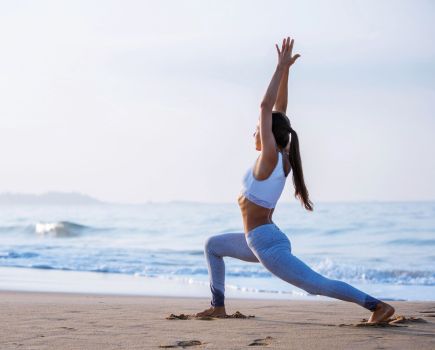 woman doing energising yoga flow workout on beach