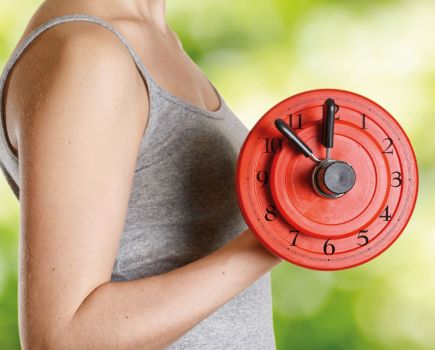 woman lifting dumbbell with clock face on, representing automaticity in fitness and how to make exercise a habit