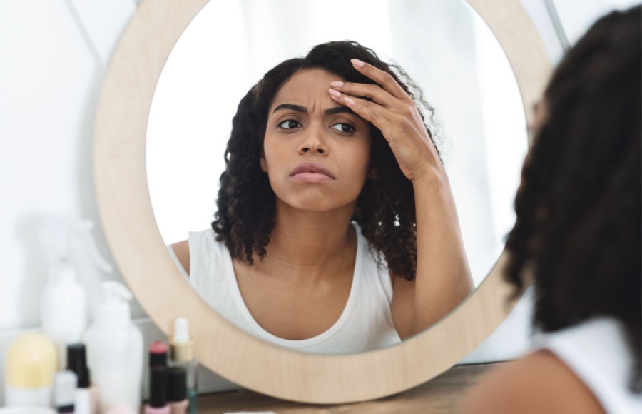 woman looks in mirror for signs of premature ageing causes