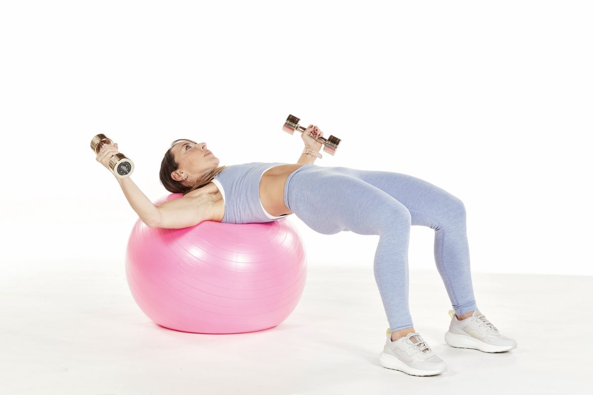 woman demonstrates chest fly on exercise gym ball
