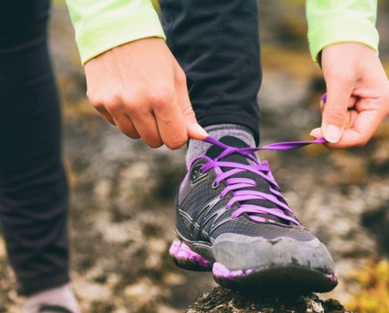 woman tying up her walking shoes during trek in woodland