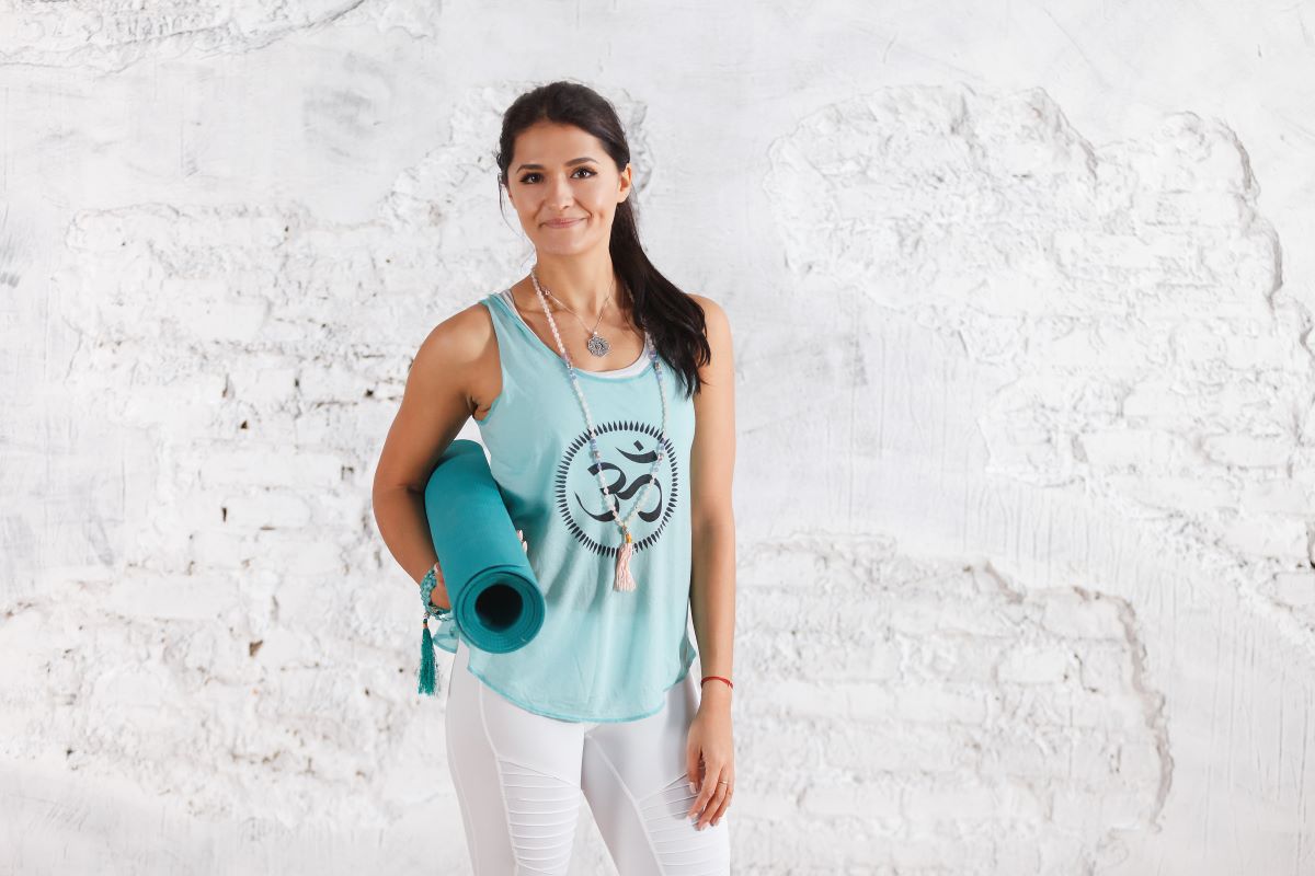 woman holding yoga mat wearing top with symbol on