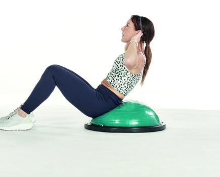 woman performs sit up exercises on bosu ball
