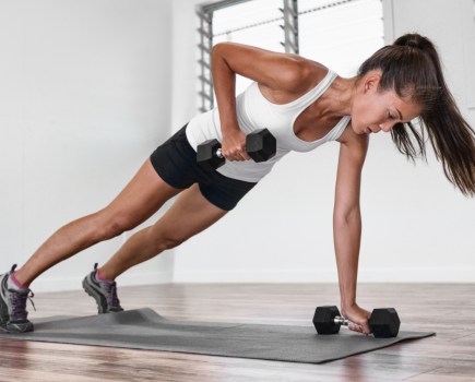 woman doing full-body hiit dumbbell workout at home on gym mat