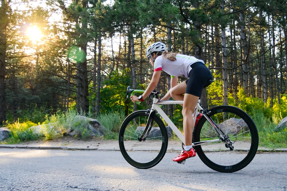 woman cycling on road through woods