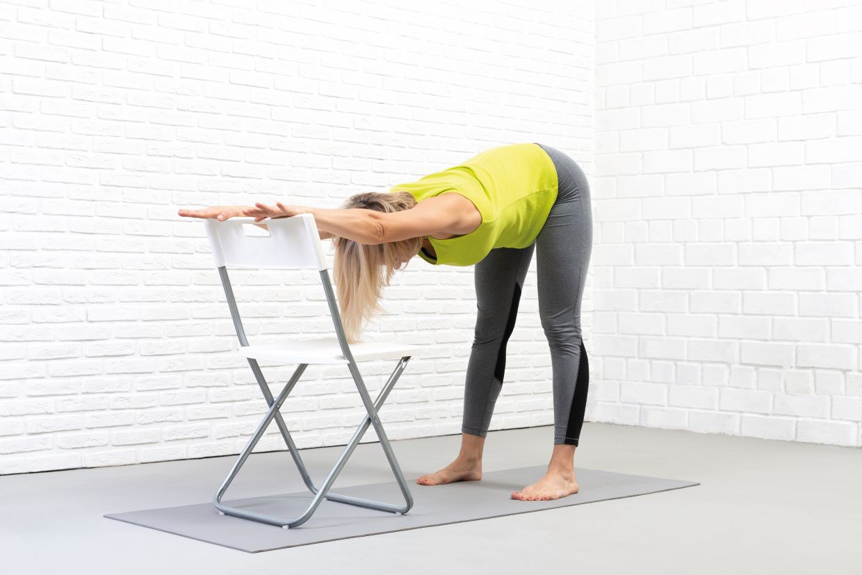 woman stretches her back using a chair for support