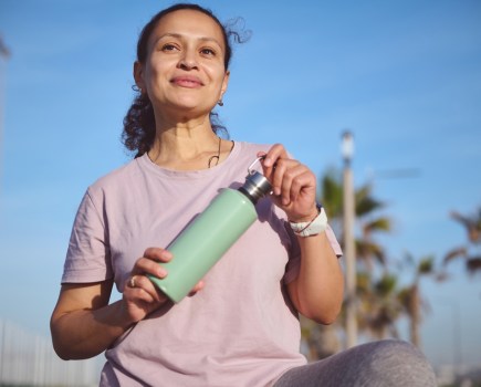 woman doing exercise outside, she is holding a water bottle and looks happy and confident, healthy habits to increase longevity and lifespan healthspan concept