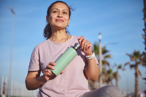 woman doing exercise outside, she is holding a water bottle and looks happy and confident, healthy habits to increase longevity and lifespan healthspan concept