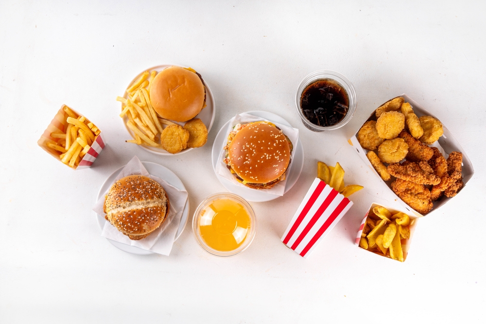 various ultra processed foods on table, including burgers, chips, crisps and fried chicken