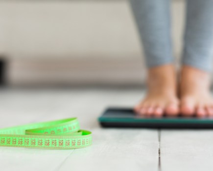 woman standing on scales measuring weight, tape measure on floor, weight loss medications fat and muscle loss concept