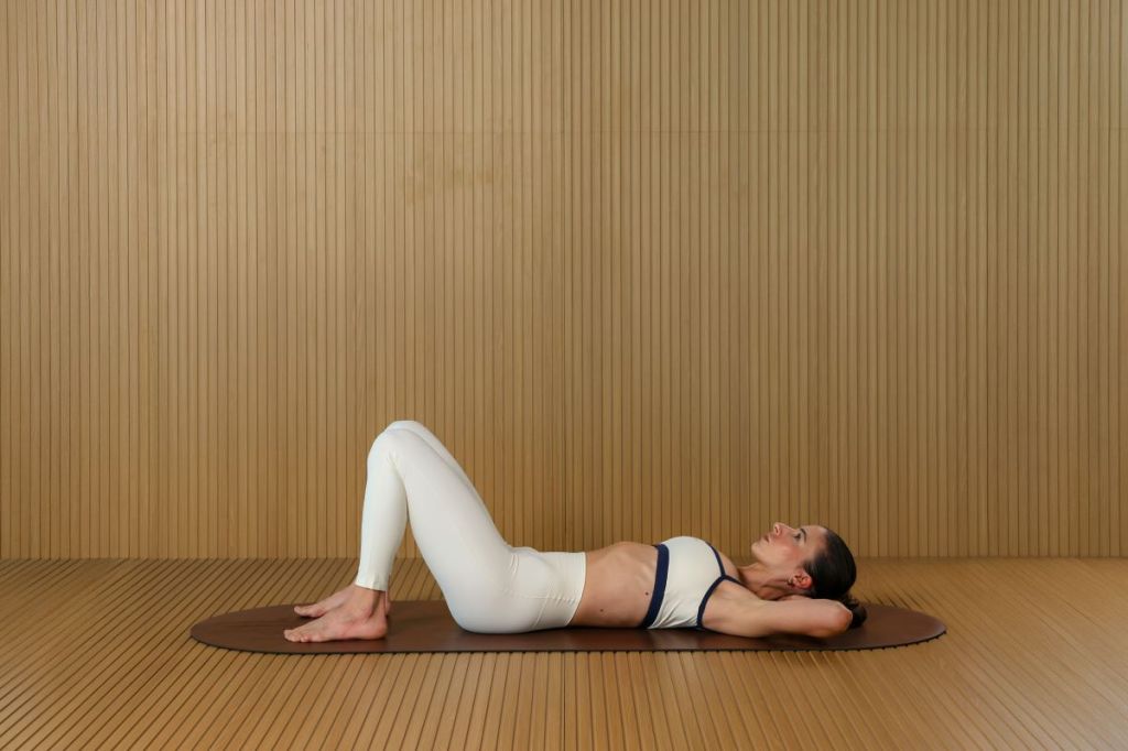 woman performs Pilates core series, lying on back with knees bent and hand behind her head