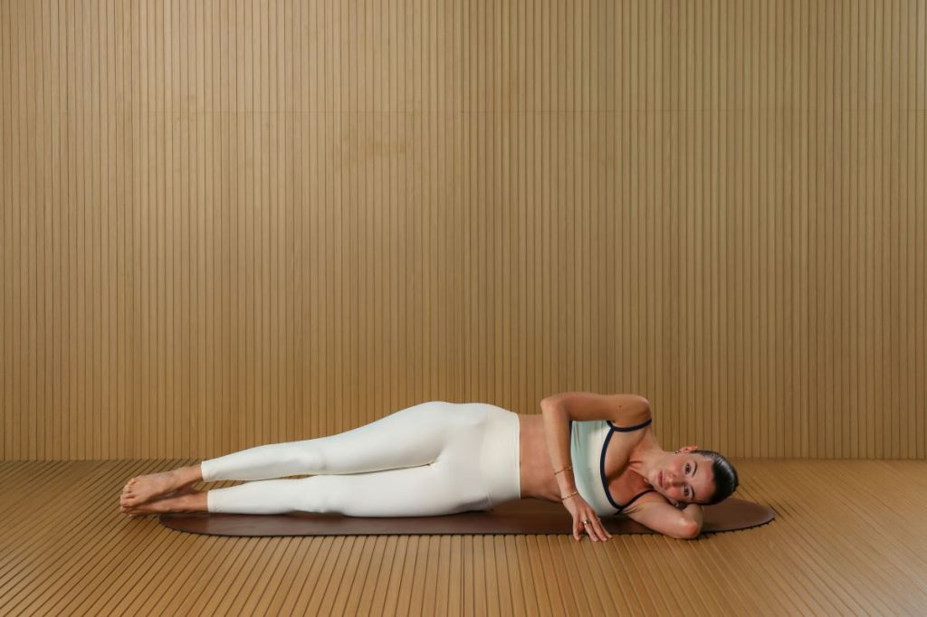 woman performs Pilates side lying sculpt move for lymphatic drainage, she is lying on her left side