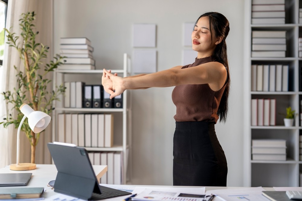 woman taking a break from working and stretching at her desk to limit pain and stiffness