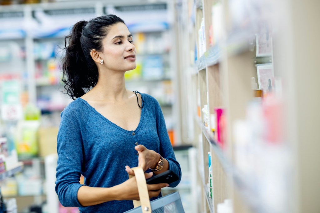 An Indian female customer selecting skincare products on a shelf inside a pharmacy.