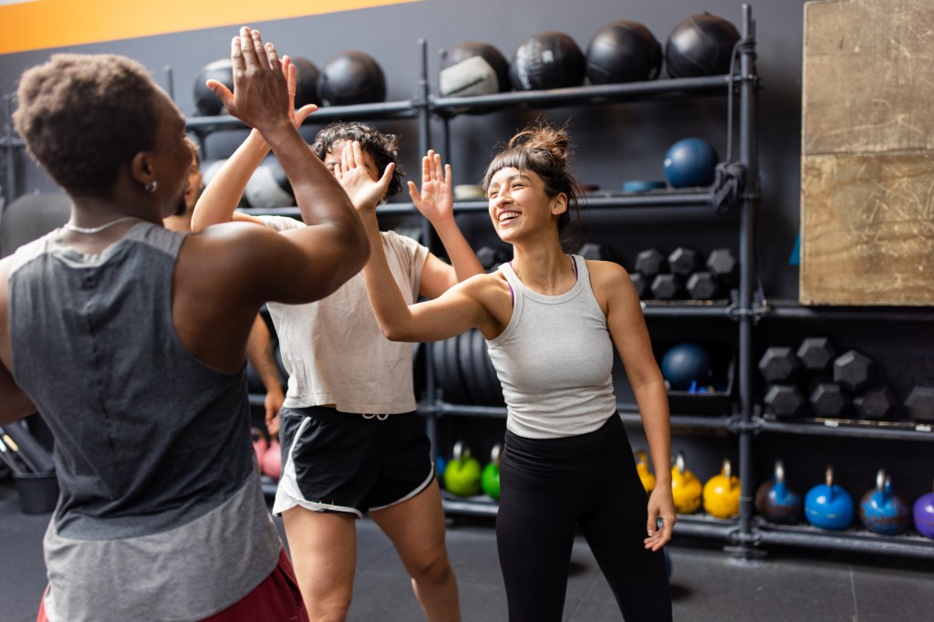 Multiracial group of young people exchanging high-fives after completing a successful workout session at a cross-training gym, fostering camaraderie and motivation.