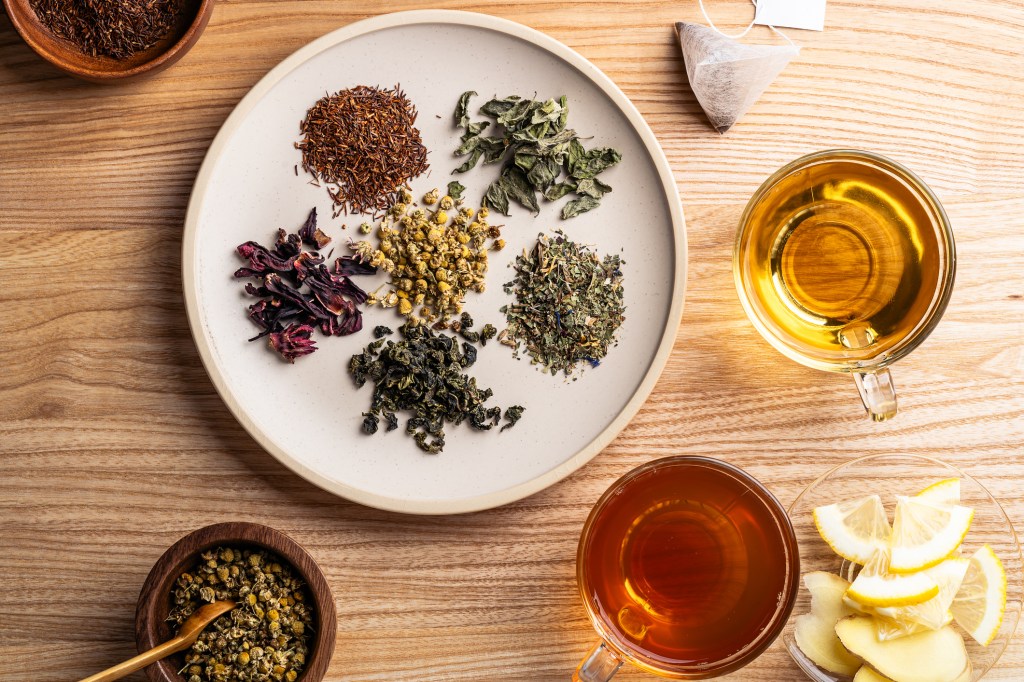 Various herbal tea leaves in plate and herbal tea in glass mug on wooden background, trending foods, superfoods